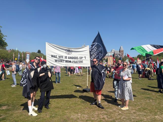 Techwerkers staan op een grasveld op het Museumplein in Amsterdam en tonen vlaggen van Tech Workers Coalition.